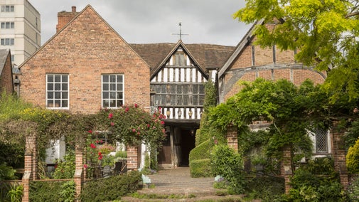 The back entrance of the red brick house at Greyfriars in Worcester surrounded by a blooming garden, hedges and flowering rose arbour